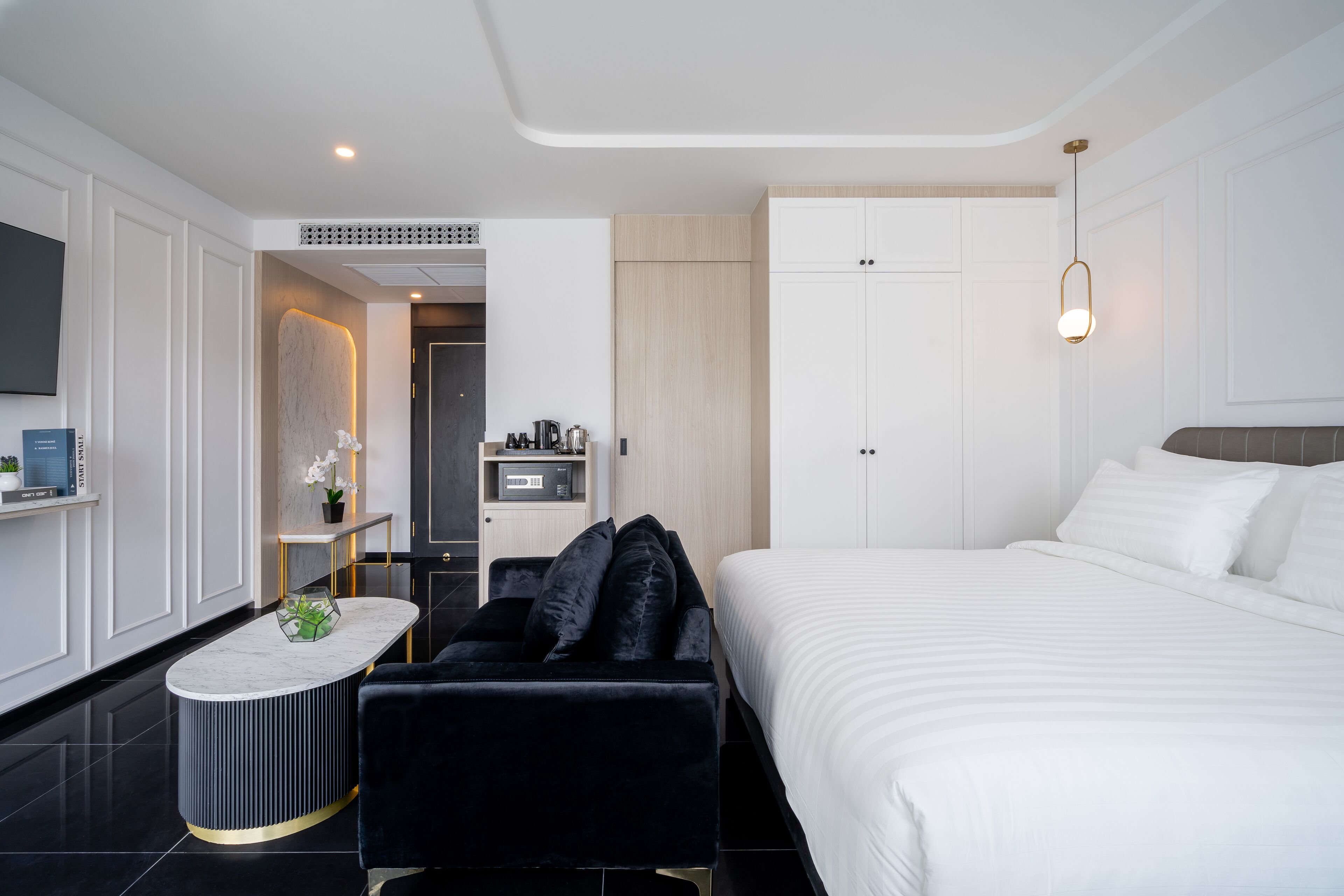 A modern hotel room with a large bed, a black sofa, a small round table, and a TV on the wall.