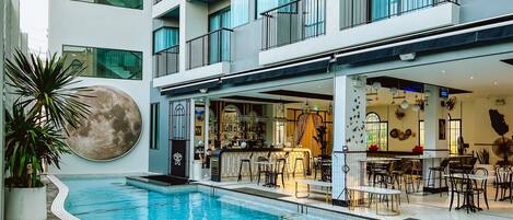 A modern hotel with a pool, outdoor seating, and a bar area.