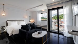 A modern hotel room with a bed, a sofa, a round coffee table, and a balcony with a city view. - Ratri Hotel Phuket Old Town (Phuket)