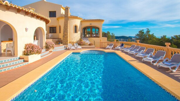 A pool area with a clear blue pool, sun loungers, and a building with arches and a balcony overlooking a scenic view. - Villa Aguila with panoramic mountain and sea views, private pool, terraces (Calpe)