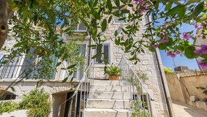 Un bâtiment en pierre avec un escalier menant à une porte, le tout entouré de verdure et de fleurs.