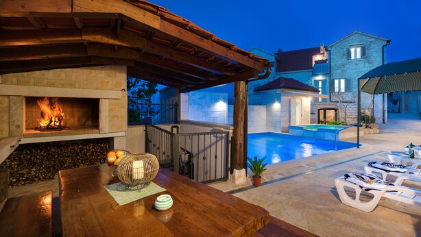Une terrasse extérieure dotée d’une cheminée en pierre, d’une piscine, de chaises longues et d’une pergola en bois.