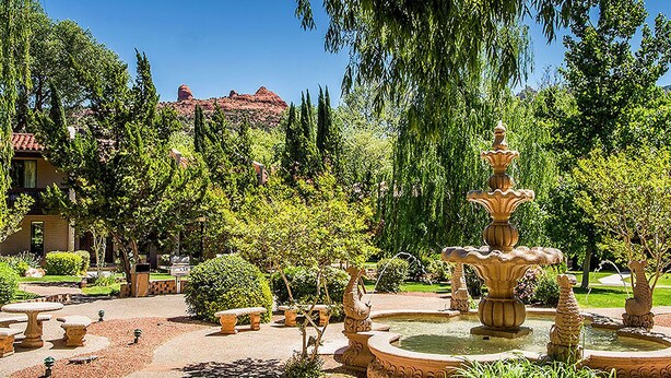Un jardín con una fuente central, rodeado de bancos ordenados y setos recortados.