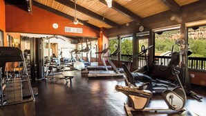 Un gimnasio con diversos equipos de ejercicio, incluyendo cintas de correr y máquinas de pesas, bajo un techo de madera con ventanas amplias que ofrecen vistas al exterior.