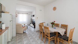 A compact kitchen with a refrigerator, stove, and dining area with a table and chairs. - Apartment Alana - (Supetar)