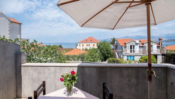A balcony with a table, a chair, a vase with flowers, and a large umbrella. - Apartment Alana - (Supetar)