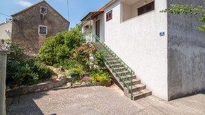 A residential building with a staircase leading to a balcony, surrounded by a garden with various plants and flowers. - Apartment Alana - (Supetar)