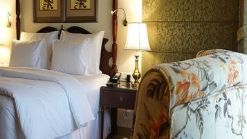 A hotel room with a double bed, a nightstand with a lamp, and two framed floral paintings on the wall.