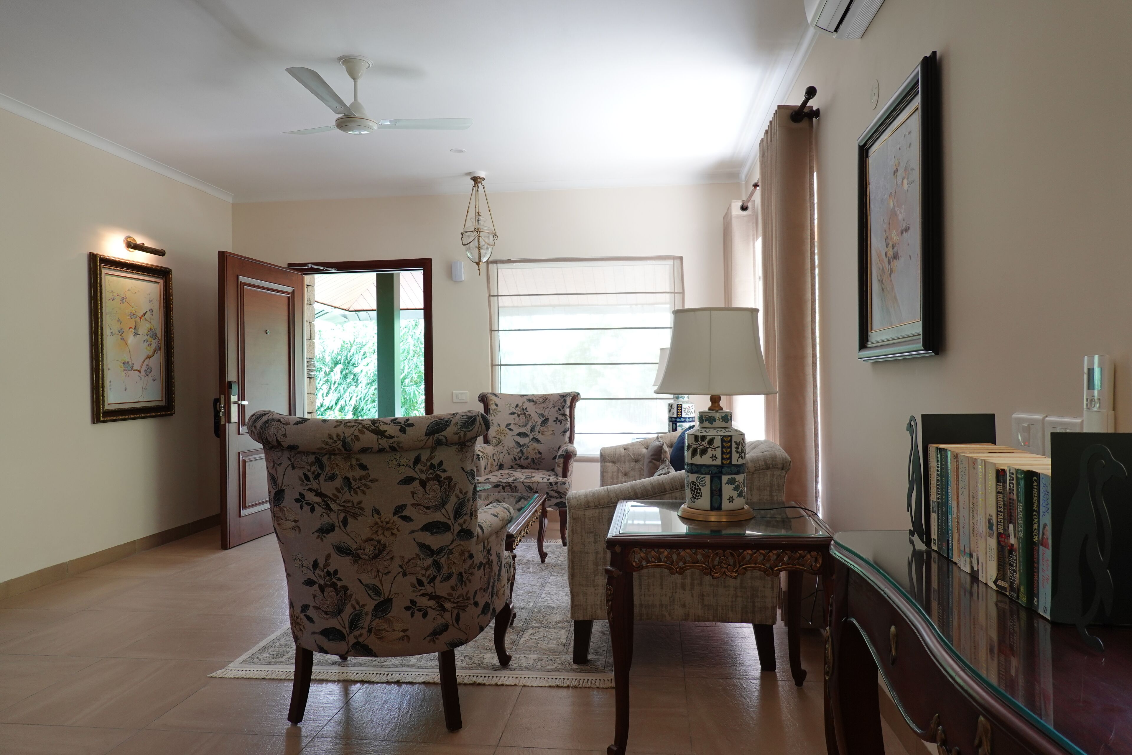 A living room with floral-patterned armchairs, a glass-top coffee table, and a bookshelf with books.