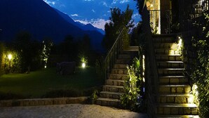 A stone staircase leading to a building with a metal railing, surrounded by greenery and a mountain in the background. - Araiya Palampur (Palampur)