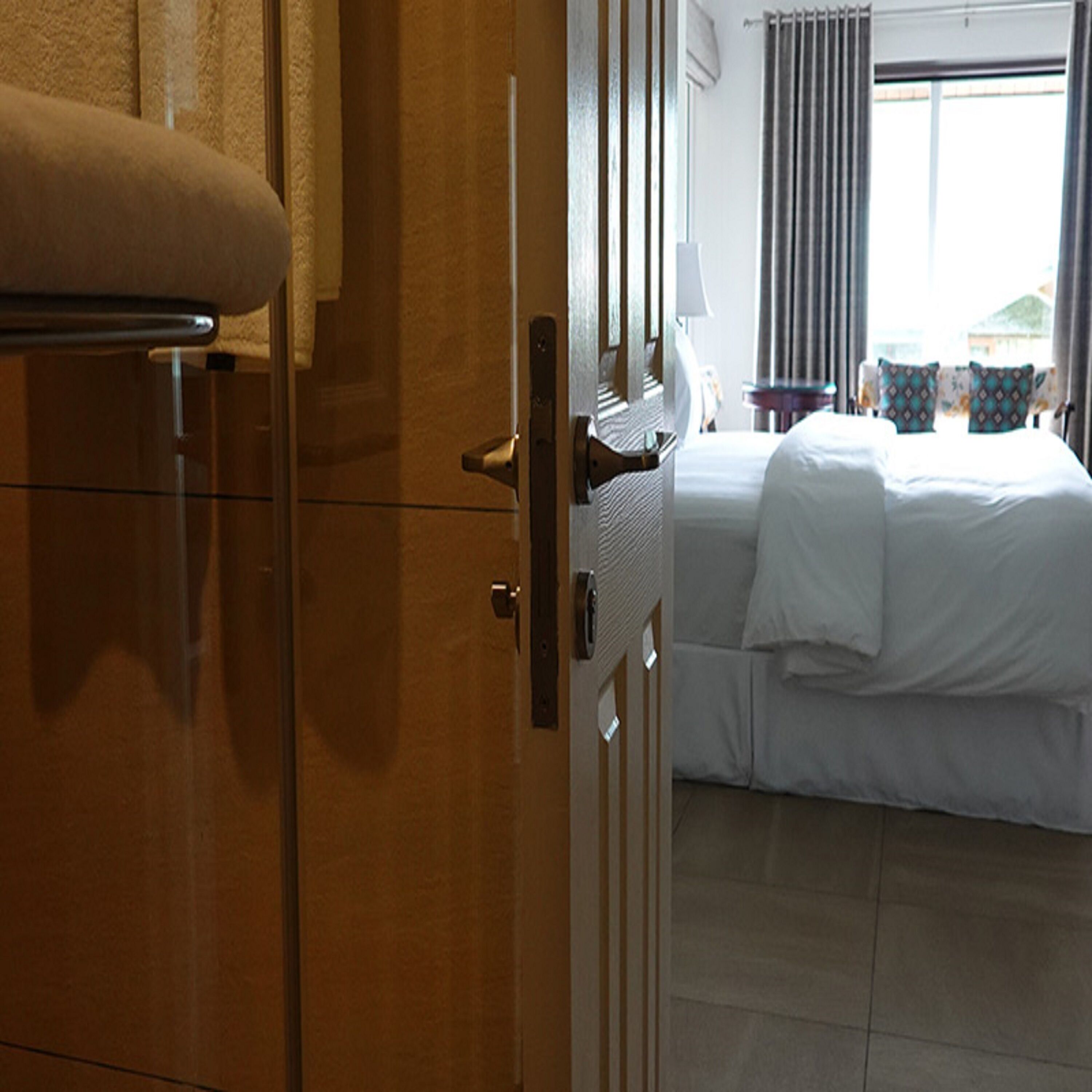 Ein Hotelzimmer mit Bett, Nachttisch, Lampe und einem Fenster mit Vorhängen.