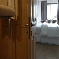 Una habitación de hotel con una cama, una mesita de noche, una lámpara y un ventanal con cortinas.
