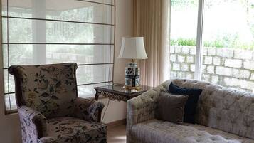 A living room with a floral armchair, a tufted sofa, a glass coffee table, and a lamp on a side table.