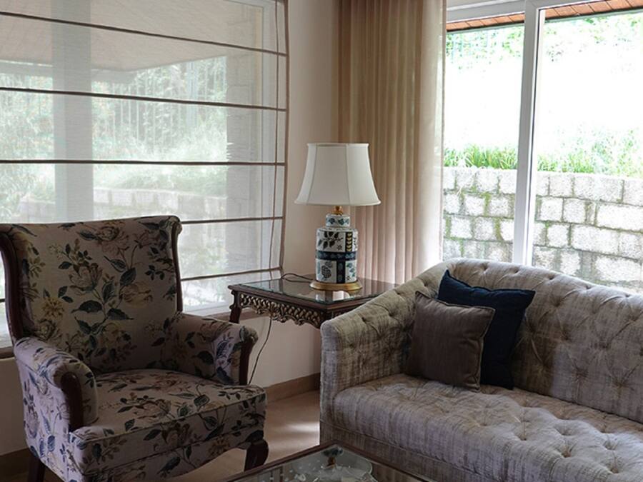 A living room with a floral armchair, a tufted sofa, a glass coffee table, and a lamp on a side table.