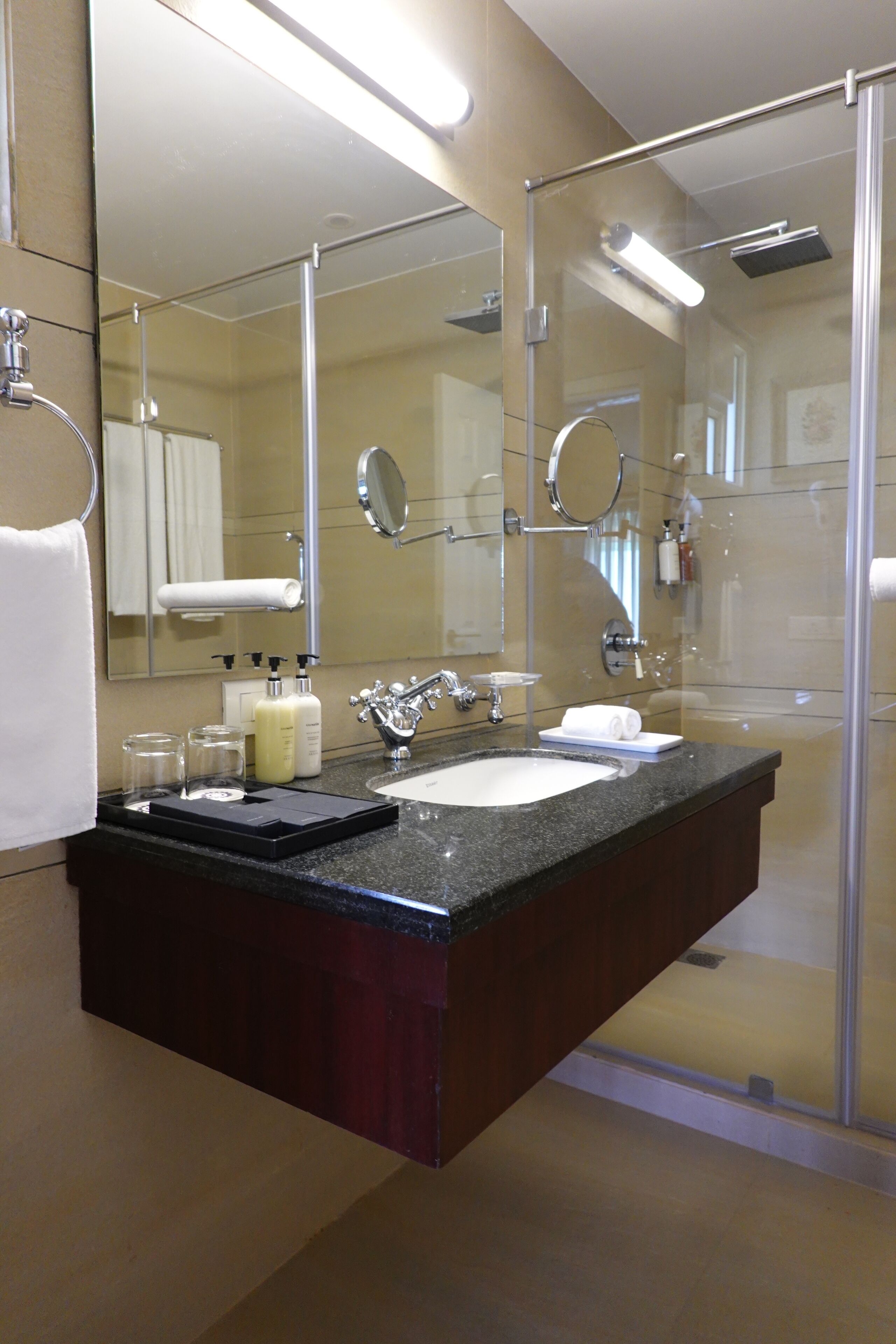 A modern bathroom with a glass-enclosed shower, a large mirror, and a marble countertop.