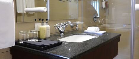A modern bathroom with a glass-enclosed shower, a large mirror, and a marble countertop.