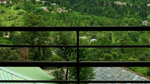 A view from a room with a sloped ceiling, looking out at a lush green valley with scattered houses and a mountain in the background. - Araiya Palampur (Palampur)