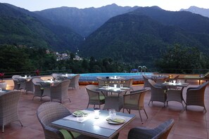 Un área de comedor al aire libre con mobiliario de mimbre y una piscina al fondo.