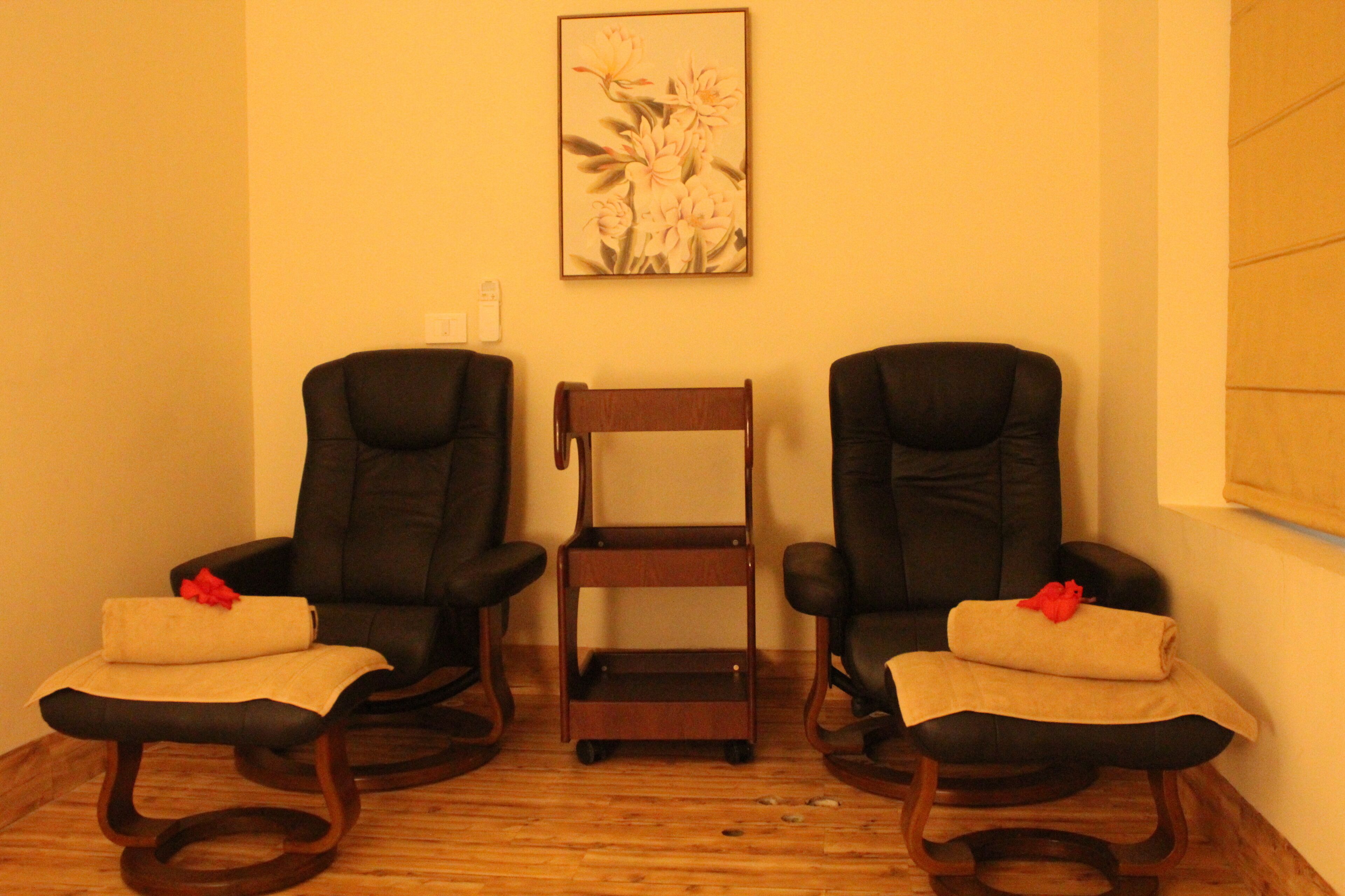 A room with two black leather chairs, a wooden side table, and a framed floral artwork on the wall.
