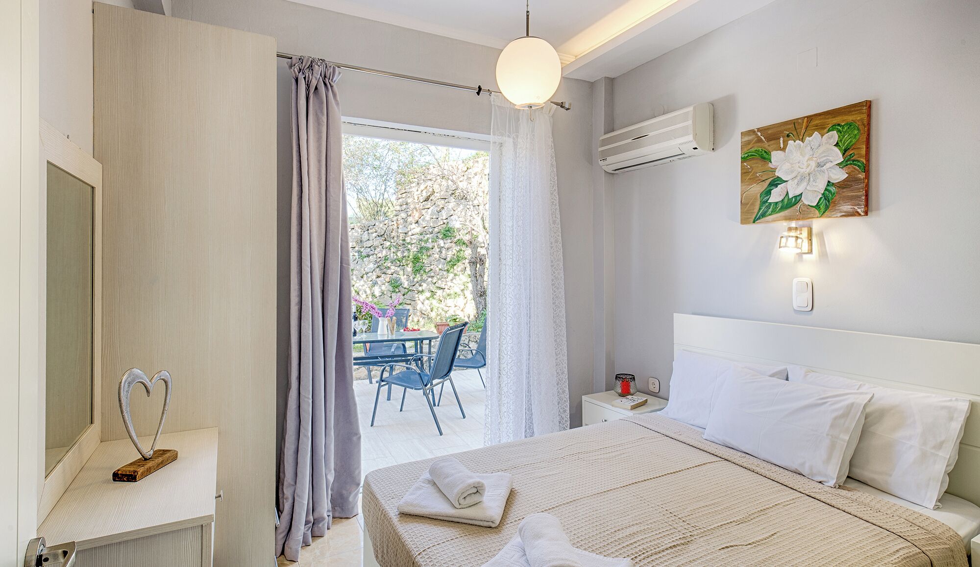 A bedroom with a bed, bedside table, and a view of an outdoor patio with chairs and a table.