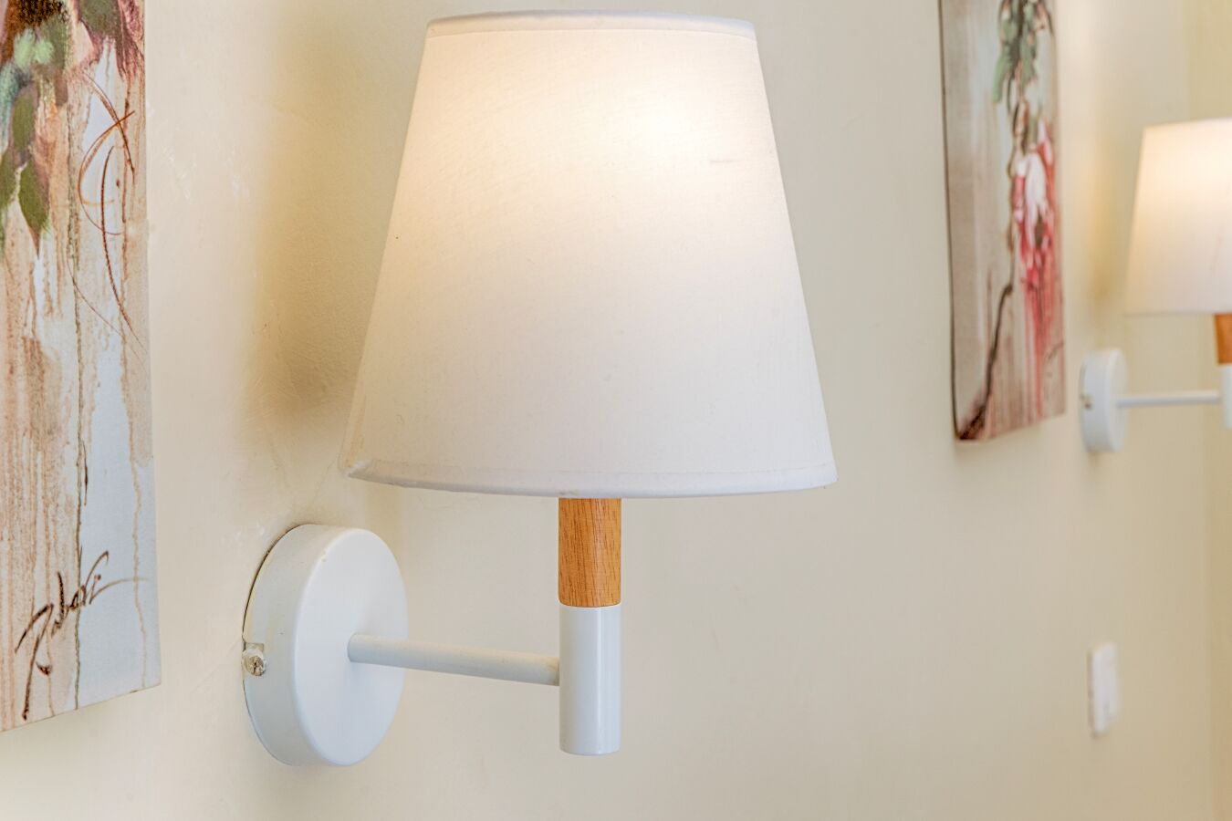 Een wandlamp met een witte kap en houten voet, geplaatst tussen twee decoratieve wandpanelen.