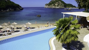 Une piscine avec vue sur la mer et une plage aménagée avec des parasols.