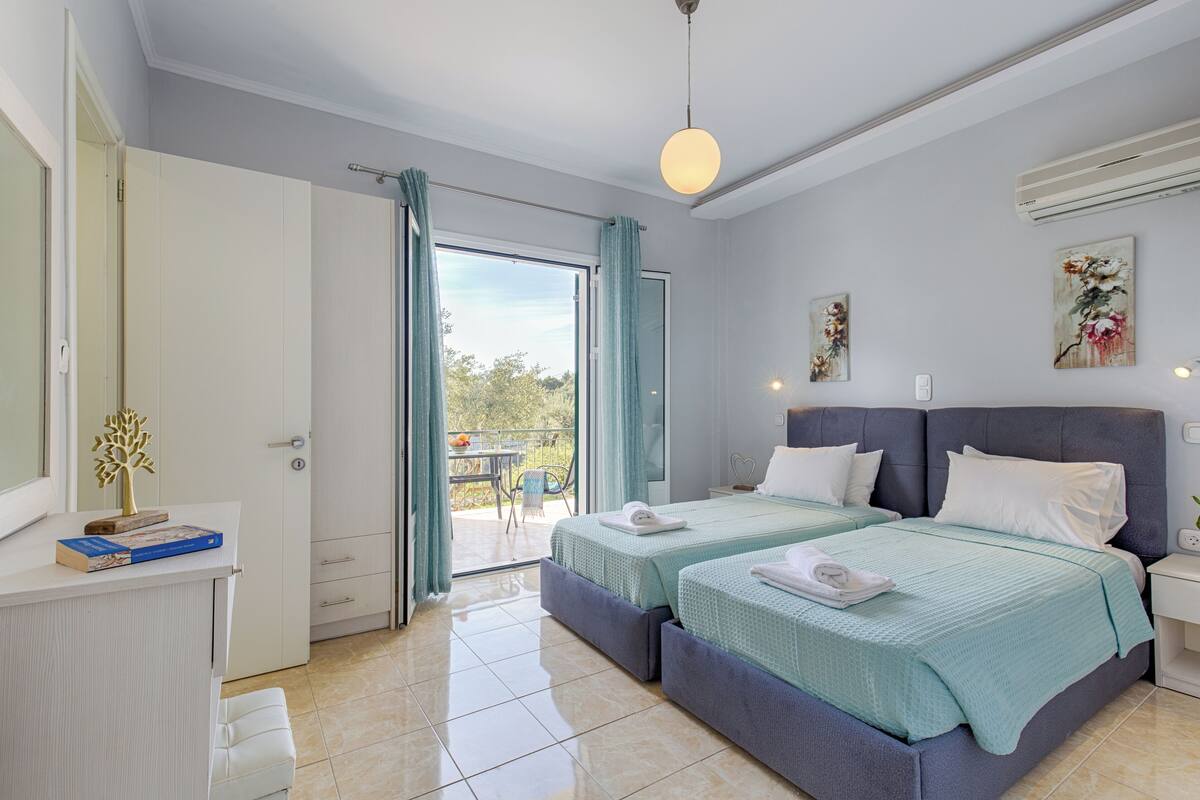 Een hotelkamer met twee bedden, een bureau en een balkon met een tafel en stoelen.