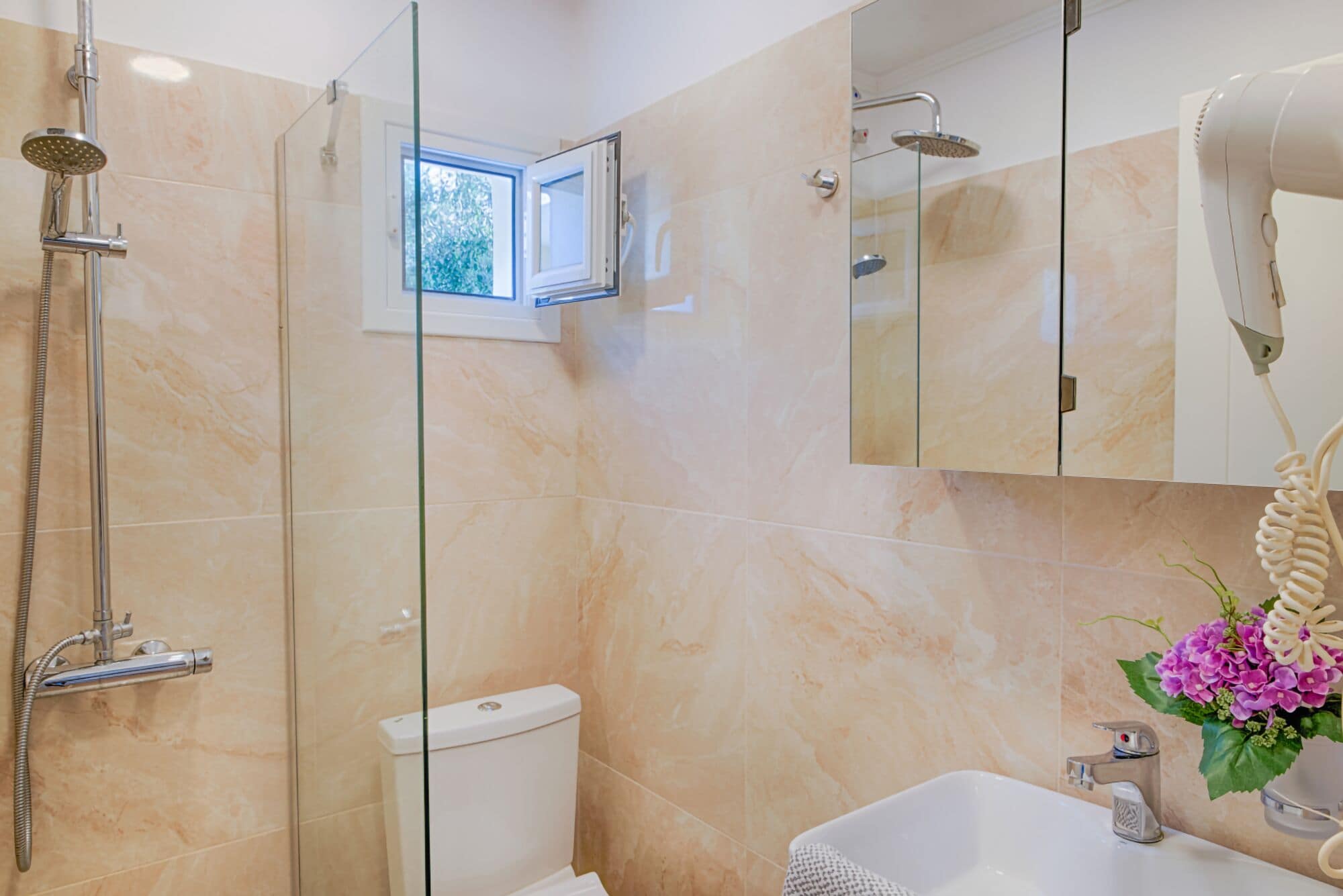 A bathroom with a glass shower enclosure, a toilet, a sink with a mirror, and a hairdryer.