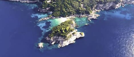 An aerial view of a coastal area with a small island surrounded by clear blue waters and dense green vegetation.