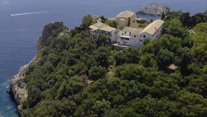Une propriété située sur la côte, avec un bâtiment blanc entouré d’une végétation luxuriante, offrant une vue sur la mer.