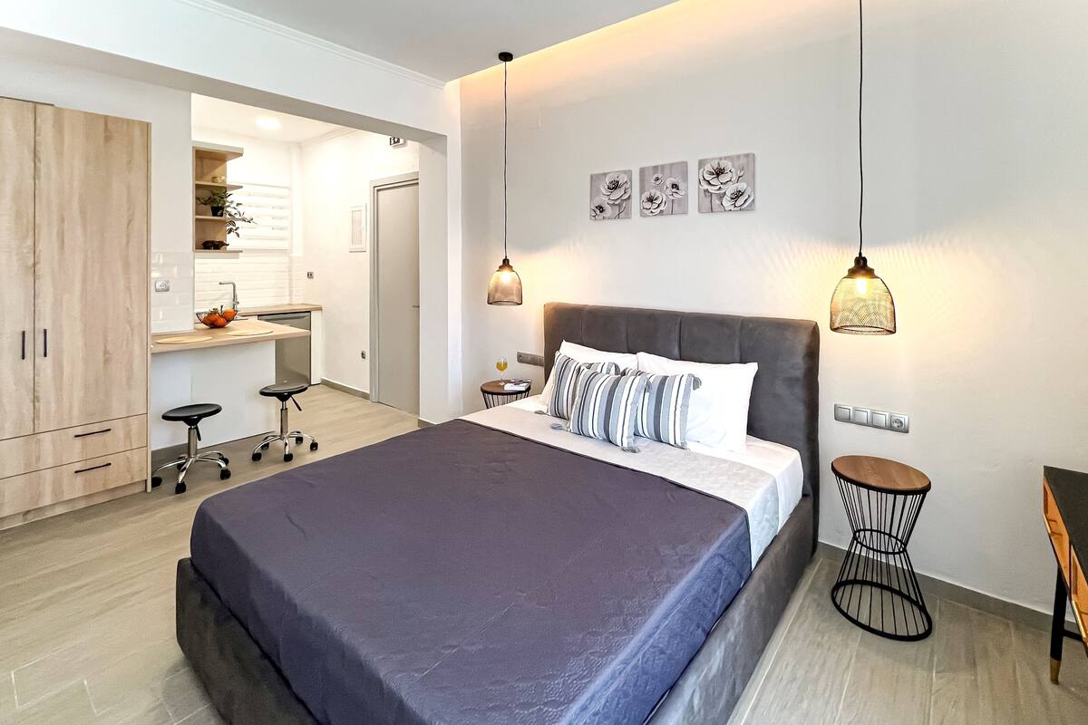 Een moderne slaapkamer met een groot bed, een bureau en een stoel. Er zijn wandlampen en een klein, rond tafeltje.