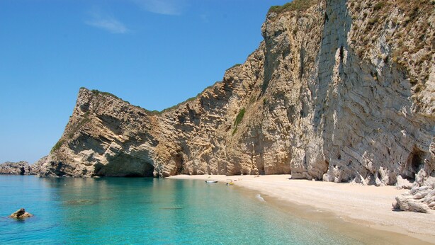 Une plage côtière aux eaux turquoise et limpides, bordée de falaises rocheuses et d’un rivage sablonneux.