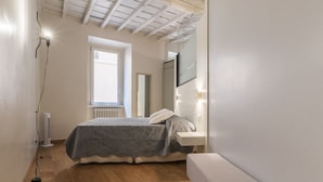 A bedroom with a bed, bedside table, bench, and a window.