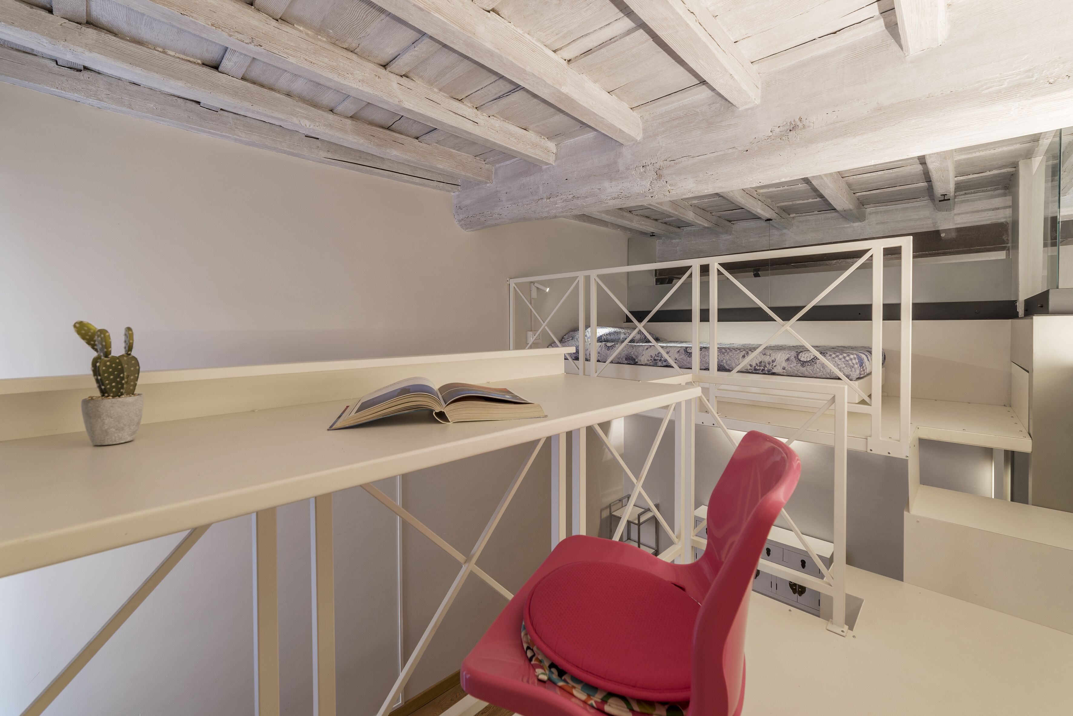 A compact room with a white desk, a red chair, a cactus, and a book.