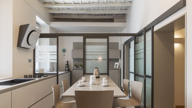 A modern kitchen with a dining table set for four, a built-in oven, and a coffee maker.