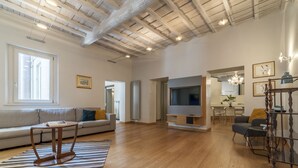 A spacious living room with a wooden floor, a large TV, and a staircase with a wooden railing.