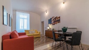 A living room with a red sofa, yellow sofa, and a dining area with a table and chairs. - Scala Santa & Laterano Open Space (Rome)