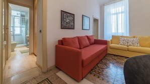 A living room with a red sofa, a yellow sofa, and a patterned rug. There are two framed pictures on the wall. - Scala Santa & Laterano Open Space (Rome)