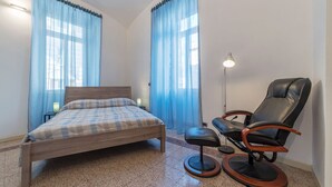 A bedroom with a bed, a chair, a lamp, and curtains. - Scala Santa & Laterano Open Space (Rome)