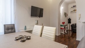 Uma sala de jantar com uma mesa, cadeiras e uma televisão fixada na parede.