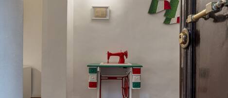 A room with a sewing machine on a green and white table, a white wall with a framed picture, and a door with a brass handle.