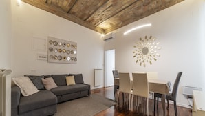 Uma sala de estar moderna com um sofá cinzento, uma mesa de jantar com cadeiras e um objeto decorativo na parede.