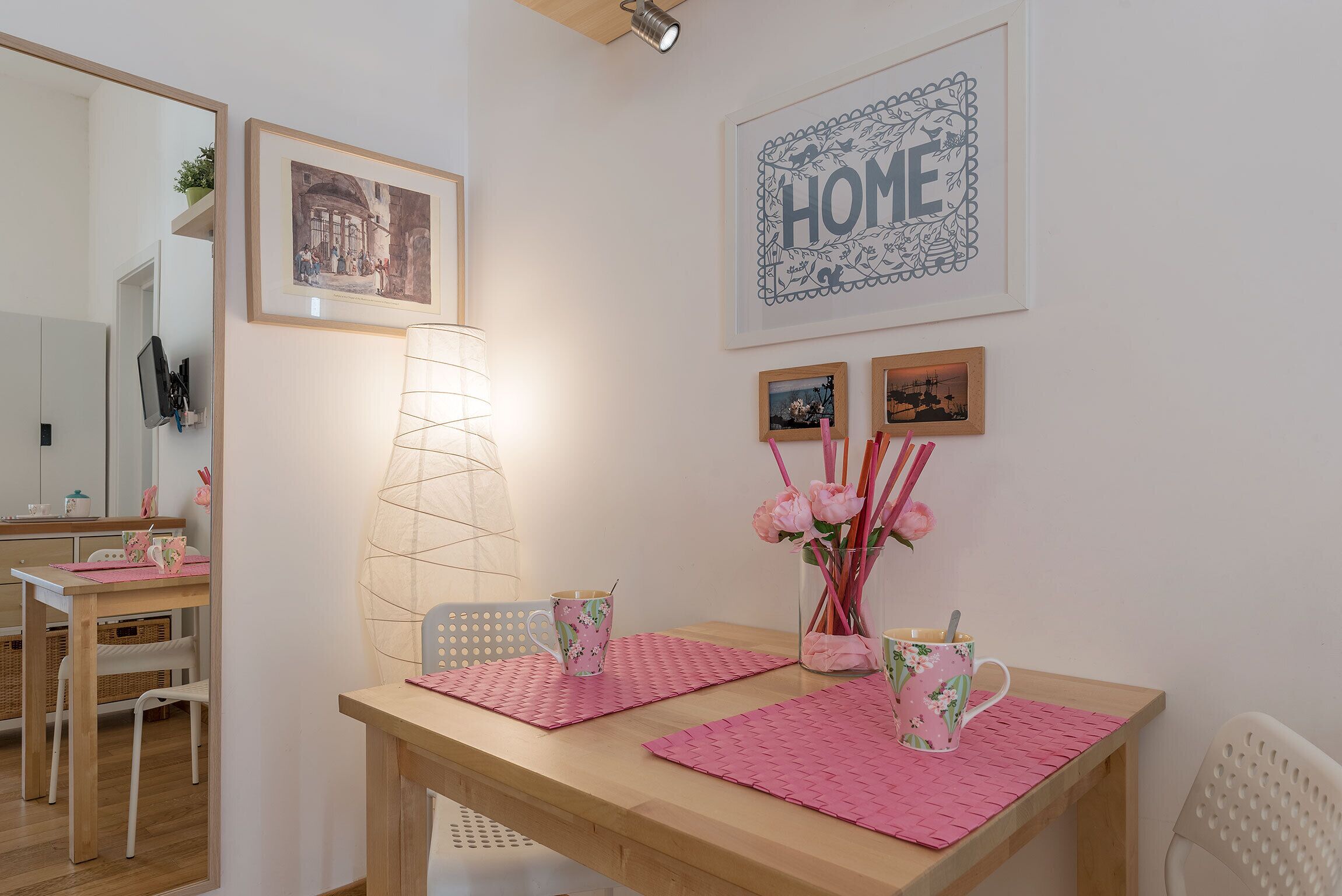 Un coin repas chaleureux avec une table en bois, des sets de table roses et des tableaux encadrés accrochés au mur.