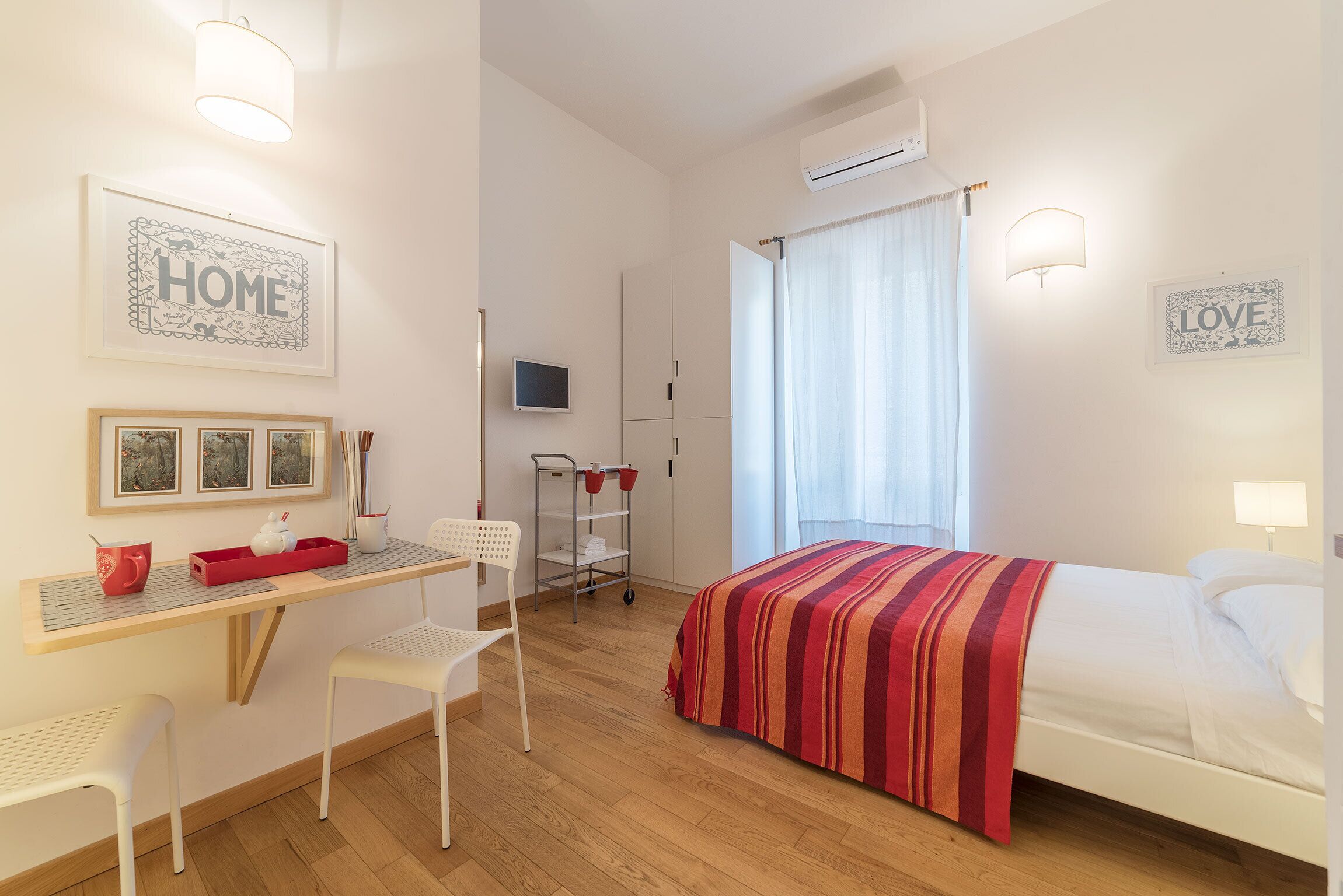 A bedroom with a bed, a desk, chairs, and a TV.