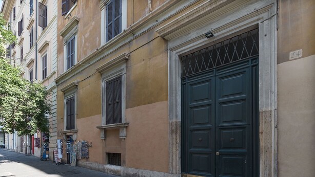 A street view of a building with a large green door, a small shop with postcards, and a tree on the sidewalk. - Santa Maria Maggiore Exclusive Apartment (Rome)