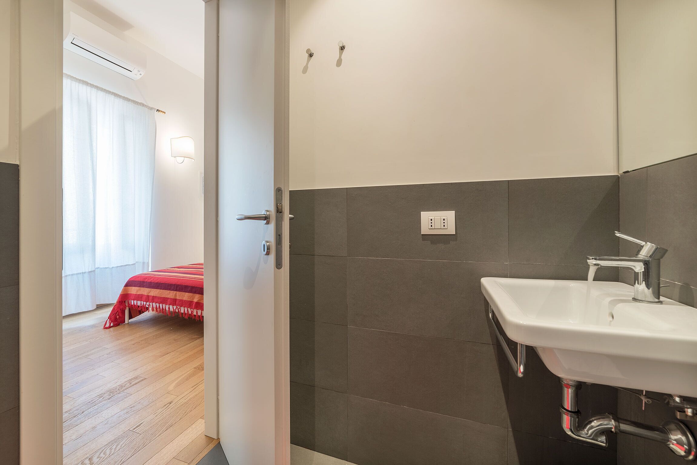 A modern bathroom with a white sink, dark tiled walls, and a wooden floor.