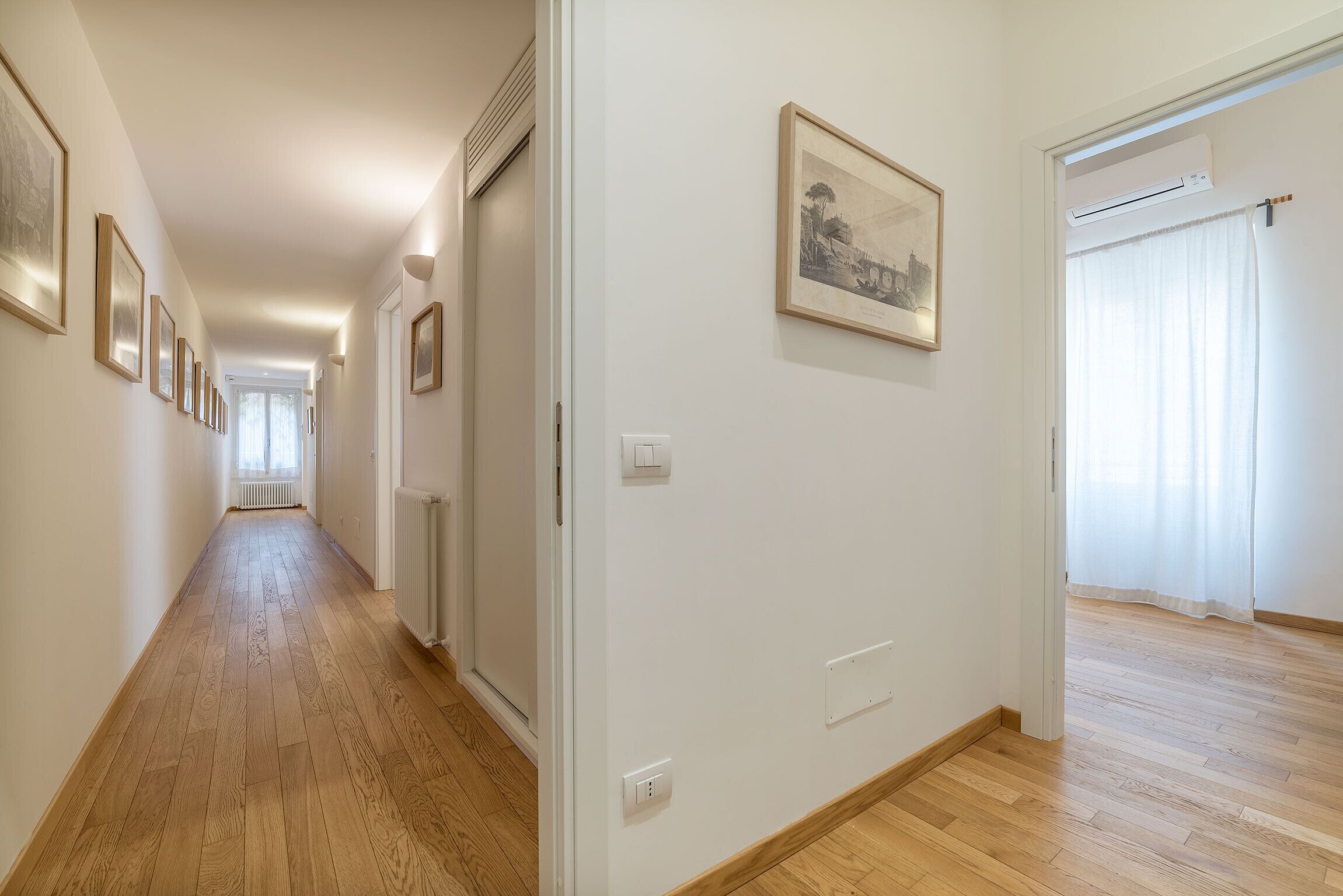 A hallway with wooden flooring, white walls, and framed artwork.