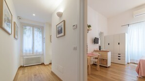 A modern, well-lit room with hardwood flooring, a white radiator, a desk with a chair, a television, and a wardrobe. - Santa Maria Maggiore Exclusive Apartment (Rome)