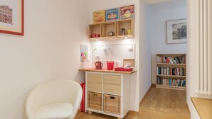 A cozy room with a white chair, a wooden cabinet with shelves, a bookshelf, and a framed picture on the wall. - Santa Maria Maggiore Exclusive Apartment (Rome)