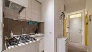 A compact kitchen with a gas stove, sink, and white cabinets. There is a small refrigerator and a yellow door in the background. - San Lorenzo Modern Flat (Rome)